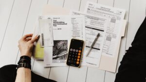 Рука з документами, калькулятором і ручкою на фоні податкових форм — символ фінансової звітності та аудиту.
